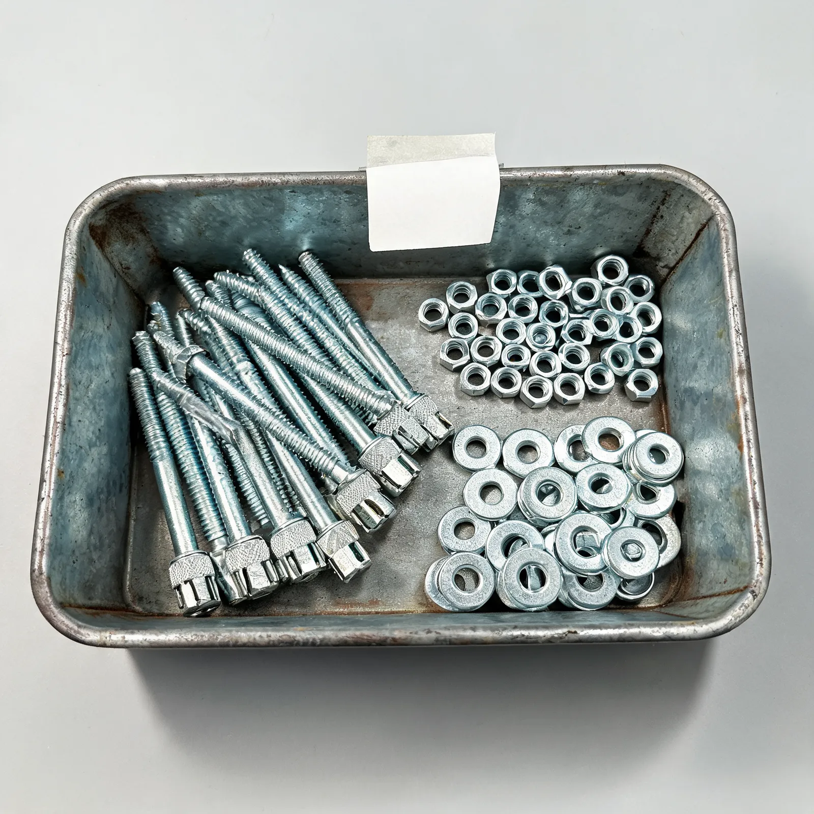 Galvanized wedge anchors and nuts arranged in a labeled metal tray under warm shop light.