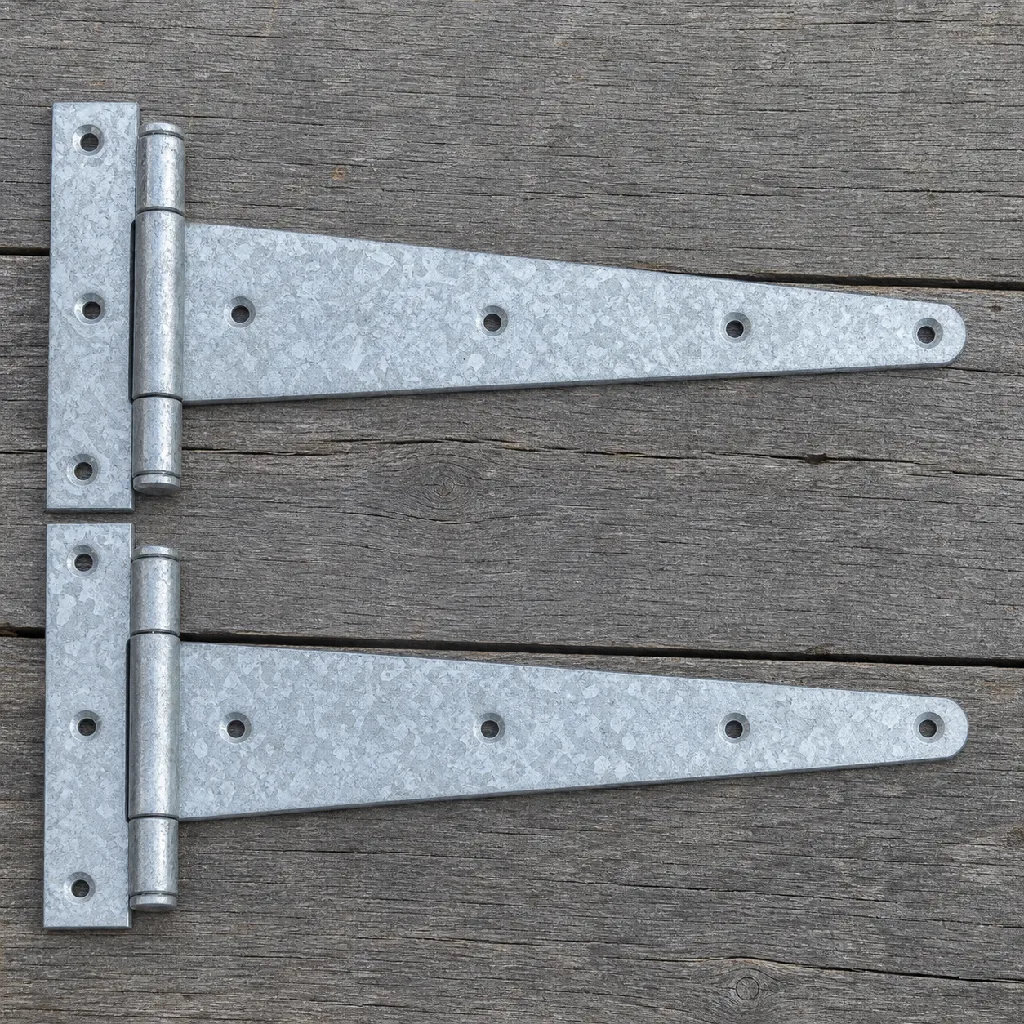 Pair of black hot-dip galvanized forged steel T-hinges laid flat on grey timber, top-down view
